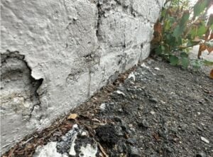 Open asphalt paving joint gap where driveway meets brick wall foundation