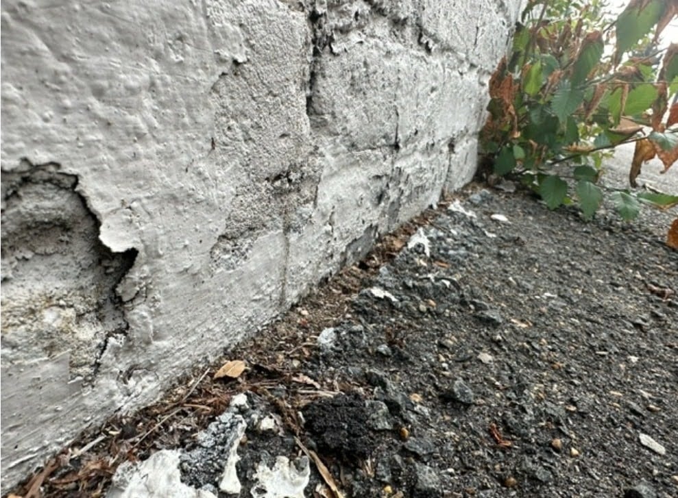 Open asphalt paving joint gap where driveway meets brick wall foundation